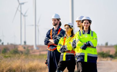 Bir grup mühendis ya da teknisyen kol kola girip sağ tarafa bakarken güzel bir kadın da kameraya bakıp yel değirmeni kümesinin önünde duruyor..