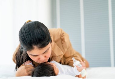 Asyalı anne, yeni doğmuş bebeğini öpüyor. Evlerinin yatak odasında sevgi ve özenle yatıyor..