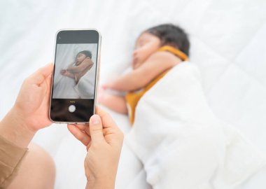 Annenin ellerini kapat. Yeni doğan bebeğinin fotoğrafını çekmek için cep telefonu kullan. Gün ışığında yatakta uyu..