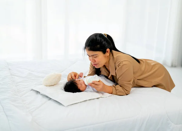 若いアジアの母親は 新生児の赤ちゃんに瓶でミルクを与えますベッドの上に横たわると彼らの家の寝室で幸せと世話をする — ストック写真