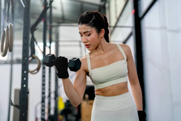 stock image Pretty Asian sport woman hold and lift dumbbell up with one hand and look to equipment in fitness gym and look concentrate to training.