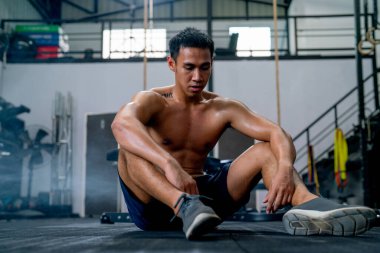 Spor salonunun önünde üstsüz oturan Asyalı sporcu egzersizin bittikten sonra spor salonunda oturuyor..