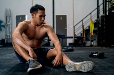 Spor salonunun önünde üstsüz oturan Asyalı sporcu egzersizin bittikten sonra spor salonunda oturuyor..