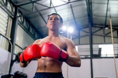 Düşük görüşlü, kırmızı boks eldivenli Asyalı sporcu kendine güvenle ayakta duruyor ve spor salonunda ileriye bakıyor..