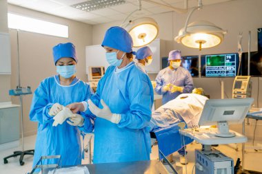 Profesyonel hemşire, ameliyat işleminden önce doktorların ameliyat eldivenlerini giymesine yardımcı olur..