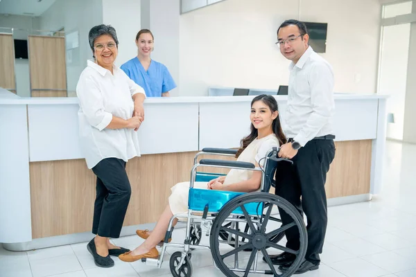 亚洲家庭有老年妇女 怀孕妇女坐在轮椅上 男子照顾妇女 她们带着护士看着相机在医院登记的背景下微笑 — 图库照片