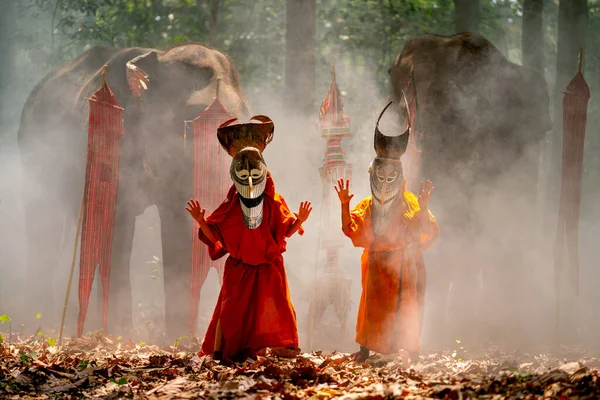 Stock image Two boy wear Pee Ta Khon, traditional culture art as ghost of Asian culture, dress and look at camera and elephants stand in the background and they stay in forest.