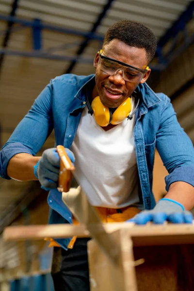 Close up African American man as carpenter use saw to cut timber in factory or workplace with happiness.