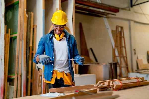 African American carpenter man use tape measure to work in factory workplace with happiness by smiling during work.