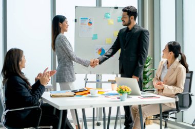 Yönetici, projenin başarısını ifade etmek için iş kadınlarıyla el sıkıştı. İş arkadaşları da bu anlaşmayı tebrik etmek için el çırptı..