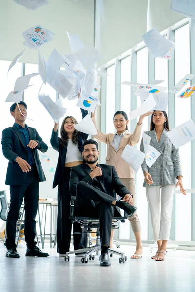 Vertical image of Asian business man and woman throw several paper up over the manager sit on chair and look at camera with confidence to show successful of the project.