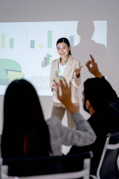 Vertical image of business man and woman raise their hands up to ask the question during presentation of Asian business woman in front of meeting room.