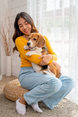 Asyalı genç kızın dikey görüntüsü. Kucaklaşın ve köpek gibi sarılın. Evinin cam kapısının önünde oturun..