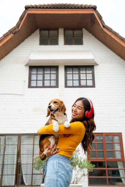 Kırmızı Kulaklıklı Genç Asyalı Kızın Dikey Görüntüsü Köpeğini Kucakla Evinin — Stok fotoğraf