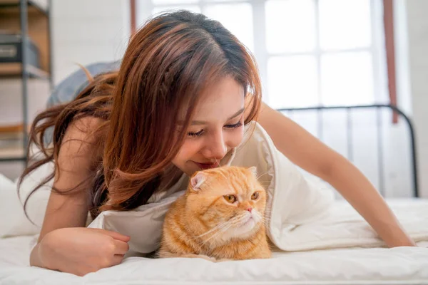 아름다운 아시아 주황색 고양이 편안하고 감정으로 침대에 고양이에게 키스한다 — 스톡 사진