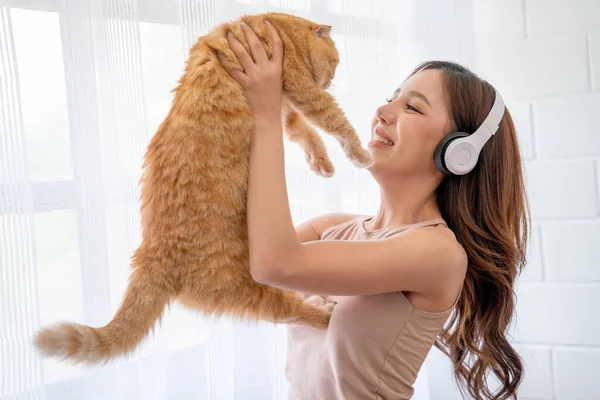 아리따운 아시아 여자는 이어폰을 커튼이 앞에서 고양이를 고행복해 보이죠 — 스톡 사진