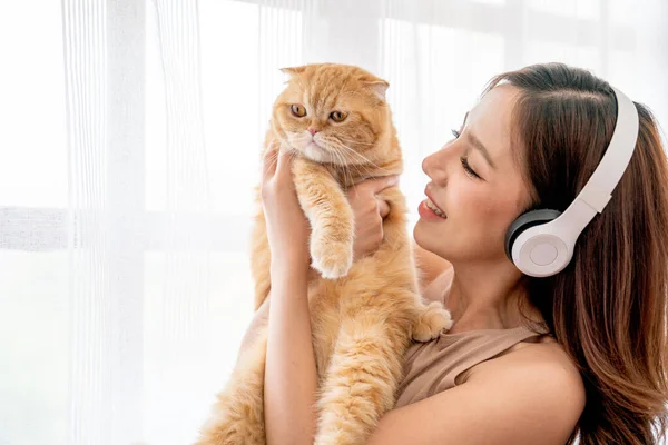 아리따운 동양인 이어폰을 커튼을 앞에서 고양이를 있으면 집에서 행복해 보입니다 — 스톡 사진