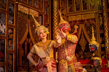 Ramakien karakterinin klasik maskeli adamı güzel Asyalı bir kadınla kırmızı maske dansında Tayland geleneksel elbisesini giy ve halka açık bir yerde Tayland tablosunun önünde dur..