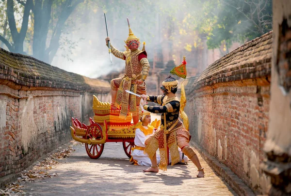 stock image Khon or traditional Thai classic masked as character of red giant stand on traditional chariot also fight to black monkey with stay in front of ancient building with mist or fog.