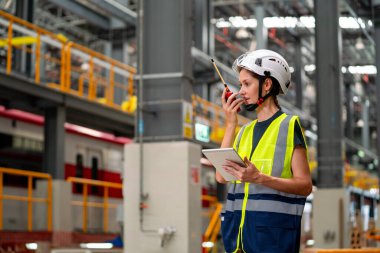 Profesyonel mühendis ya da teknisyen kadın tablet tutuyor ve telsizle diğer ekip çalışanları ile iletişim kuruyor ve fabrika sanayi işyerinde kalıyor..