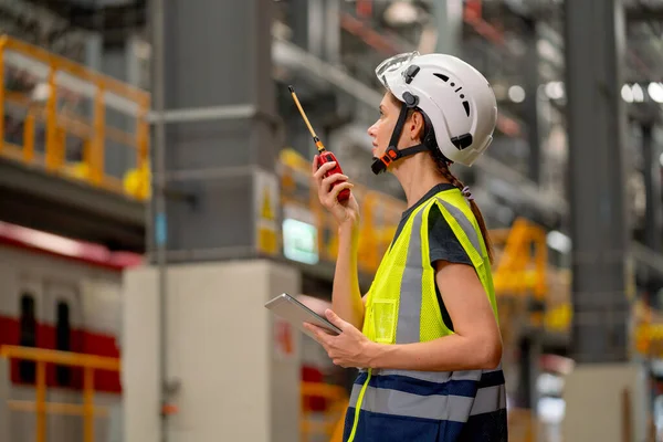 Pretty factory worker woman use walkie talkie to contact with team or co-worker and also hold tablet in concept of happiness and good system to work in workplace of industrial center.