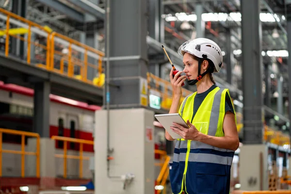 专业工程师或技术员妇女手持平板电脑 使用对讲机与团队中的其他同事交流 并呆在工厂行业的工作区 免版税图库照片