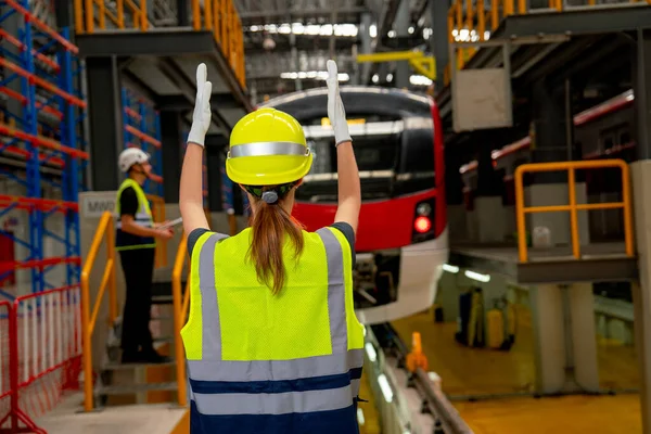 Back of technician or factory worker woman stand and show action to the driver in electric train in factory workplace and co-worker also stay near the train.