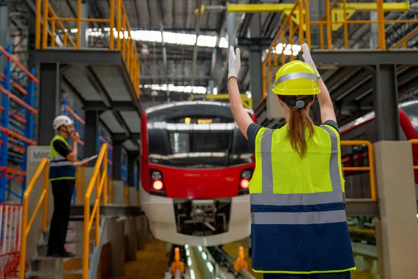 Technician or factory worker woman stand and show action to the driver in electric train in factory workplace and co-worker also stay near the train.