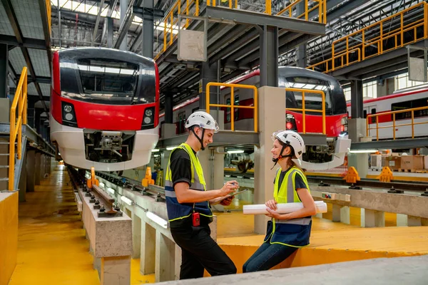Technician or engineer workers man and woman stay in front of electric train and they look happy during work or relax in factory workplace.