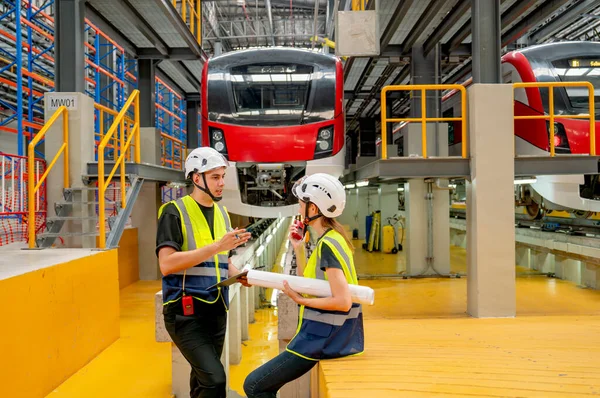 Professional technician or engineer workers man and woman stay in front of electric train and they look happy during work or relax in factory workplace.