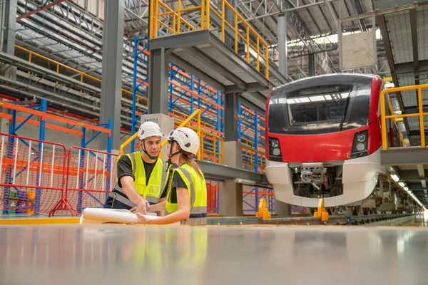 stock image Two engineer or technician workers man and woman discuss together using drawing paper and stay in area near rail and front of electric train.