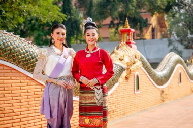 Tayland geleneksel elbiseli iki Asyalı kadının portresi, güzel sanat ve mimari ile antik pagoda yolunda yan yana duruyor, ayrıca gülümsüyor ve kameraya bakıyorlar..