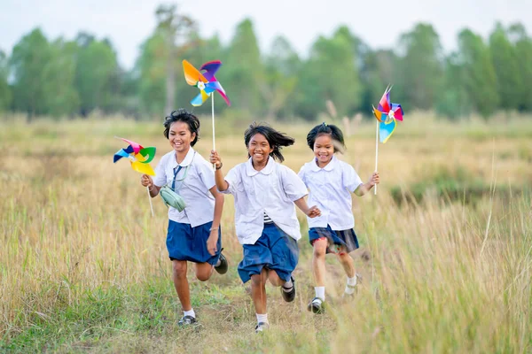 小さなアジアの少女の側面の景色は小さな風車を保持し 田んぼの散歩道で一緒に走るのが楽しいように見えます — ストック写真