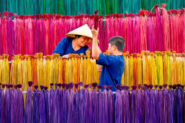 Asian boy help senior woman to work with multicolor dry weed that use for making mat or wicker and they look happy to work together.