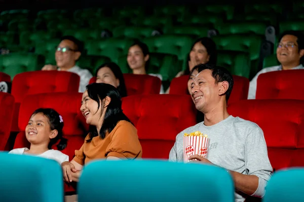 Asian family with father, mother and daughter enjoy and happy to watch movie together in cinema theater and they smile in concept of family time for relax on holiday.