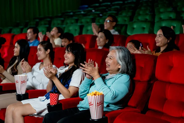 Wide shot of multiethnic and multigeneration people clap hands during watch movie together in cinema theater and they look happy in concept of enjoy entertainment on holiday.