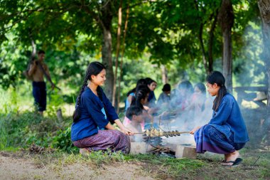 İki Asyalı kız pirinç tarlasında çiftçilik yaparken ya da tarlada çalışırken Asyalı çiftçilerin önünde ızgara balık yapmış ve birlikte çalışmaktan mutlu görünüyorlar..