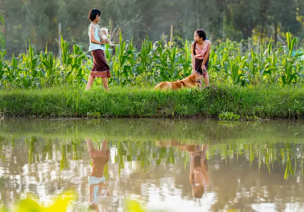 Young Asian woman hold and carry cat and walk to talk with her friend who stay with dog near water reservoir and the reflection also show in surface of water.