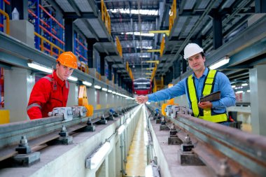 Profesyonel mühendis görünüş ve kamera tableti de tutuyor ve fabrika işyerindeki elektrik veya gökyüzü treninin demiryolu kenarındaki teknisyenleri işaret ediyor..