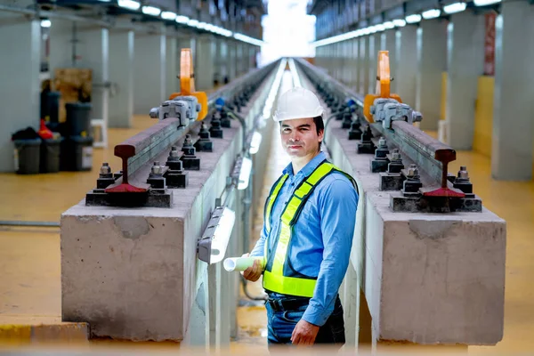 Portrait of professional engineer stand between railroad tracks of electrical or sky train in the factory workplace.