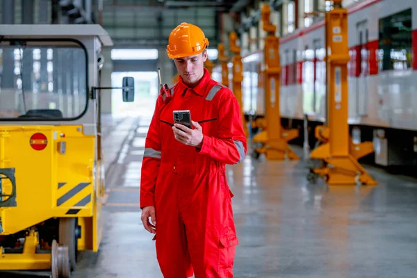 Professional technician worker stand and hold with looking at mobile phone in electrical or metro train factory. Concept of communication during work in industrial workplace.