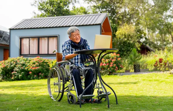 Senior man sit on wheelchair enjoy and relax with laptop outdoor in the garden with warm light.