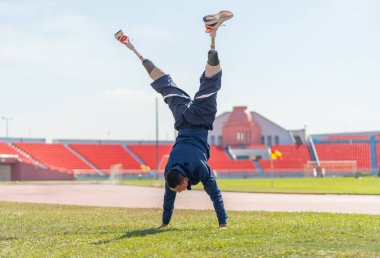 Bacağında protezi olan sporcu bir sporcu. Vücudu ısıtıyor. Stadyumdaki çimenlik alanda gün ışığında amuda kalkıyor..