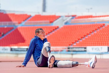 Bacağında protezi olan sporcu bir sporcu stadyumdaki egzersizden sonra rahatlamak için piste oturur. Spor konsepti.