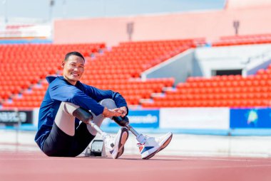 Sporcu sporcu protez bacakları pistte oturur ve stadyumdaki egzersizden sonra gülümseyen kameraya bakar. Spor konsepti.