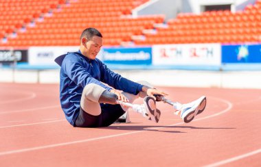 Sporcu sporcu protez bacakları stadyumda gün ışığıyla ayakta oturuyor ve mutlu görünüyor..