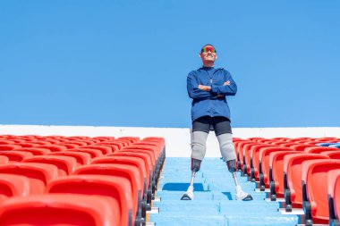 Sporcu atlet protez bacakları merdivenlerde kolları bağlı, stadyumdaki amfi tiyatroda gün ışığında mutluluk içinde ayakta duruyor..