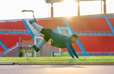 Bacağında protezi olan sporcu bir sporcunun yan görünüşü uzanır ve bir bacağını geriye ve yukarı uzatır ayrıca stadyumdaki antrenmandan önce ısınmak için sabırsızlanır..