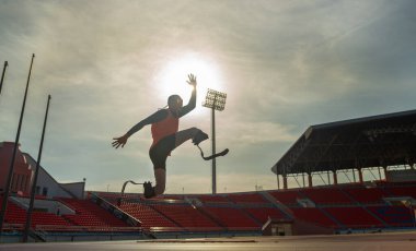 Spor adamı protez bacakları stadyumun öğleden sonra güneş ışığının önüne atlıyor..