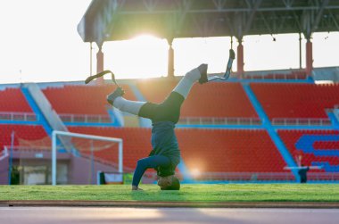Sporcu atlet protez bacakları çimenlikte başı itmek ve akşamları hafif ışıkla stadyumda bacaklarını ayırmak..